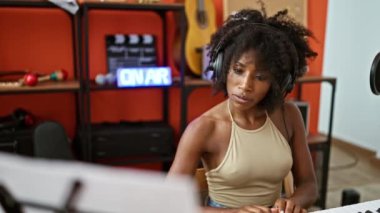Piyano çalan Afrikalı Amerikalı kadın müzisyen müzik stüdyosunda kulaklıklarını çıkartıyor.