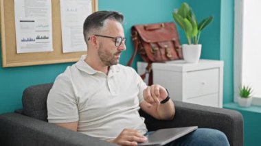 Gri saçlı iş adamı. Bilgisayarı açıyor. Ofise bakıyor.