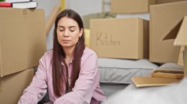 Genç, güzel, İspanyol bir kadın yeni evinde karton kutuları açıyor, sarılıyor.