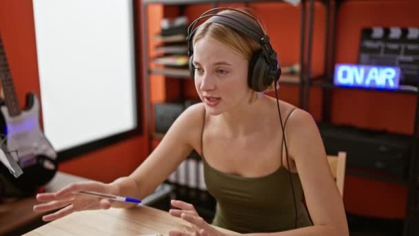 ポッドキャストスタジオで話すノートを取る若い金髪女性ラジオレポーター — ストック動画