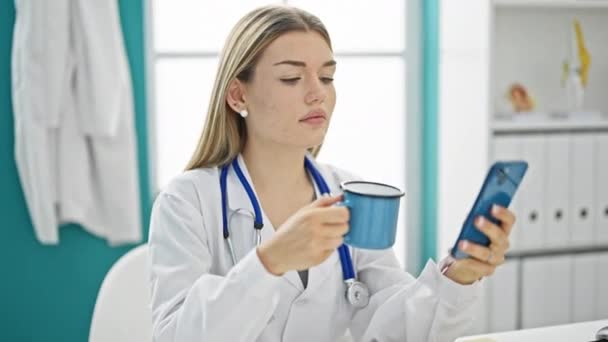 年轻的金发女医生在诊所用智能手机喝咖啡 — 图库视频影像