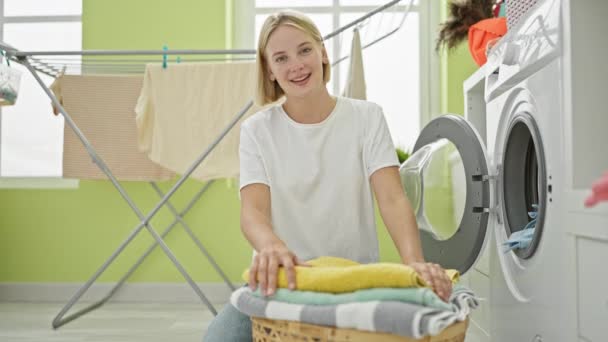若い金髪の女性は 洗濯室で折り畳まれたタオルに自信を持って微笑みます — ストック動画
