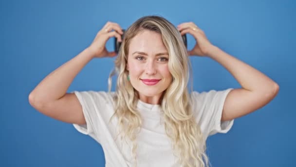 Mujer Rubia Joven Sonriendo Confiada Usando Auriculares Sobre Fondo Azul — Vídeos de Stock