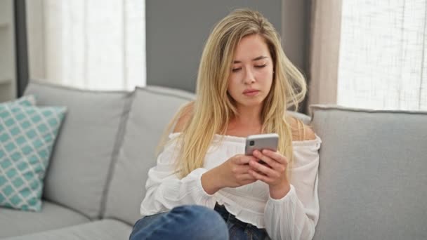 Jeune Femme Blonde Utilisant Smartphone Assis Sur Canapé Regardant Bouleversé — Video