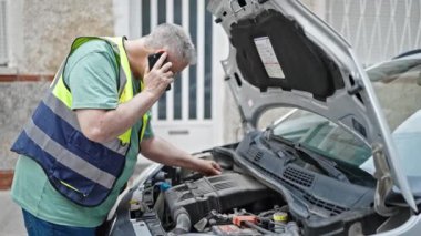 Orta yaşlı, kır saçlı, akıllı telefondan konuşan, sigortalı arabaları tamir eden bir adam.