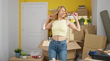 Genç sarışın kadın gülümsüyor. Kendine güveni tam. Yeni evinde kazanan bir jestle duruyor.