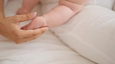 Anne ve kızı yatak odasında birlikte oturup ayaklarına dokunuyorlar.
