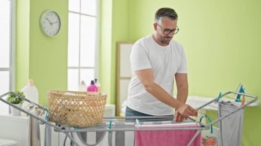 Gri saçlı, gülümseyen, kendine güveni tam çamaşırhanede çamaşır ipine asılı duran bir adam.