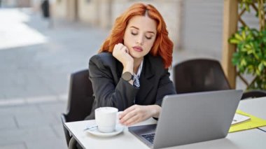 Genç kızıl saçlı iş kadını laptopunu kullanıyor. Kahve dükkanının terasında kahve içiyor.