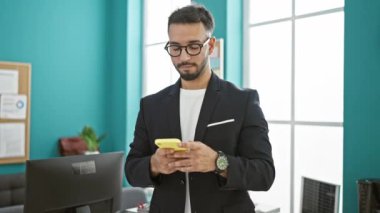 Genç Arap iş adamı ofiste akıllı telefon kullanarak gülümsüyor.