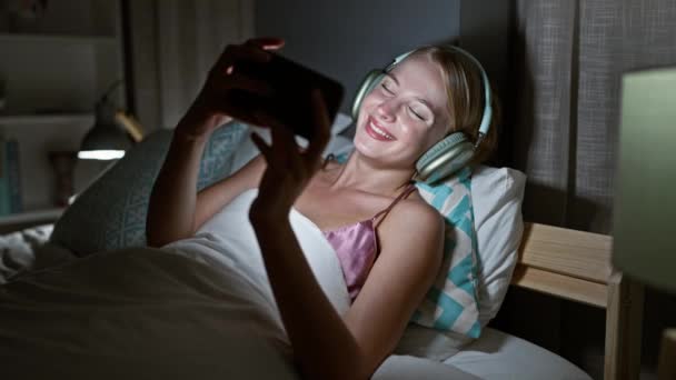 금발의 여자가 스마트 비디오를 침실에서 침대에 — 비디오