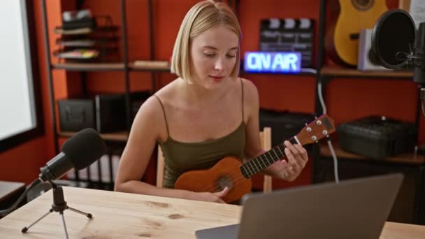 若いブロンドの女性ミュージシャン 音楽スタジオでオンラインウクレレレレッスン — ストック動画