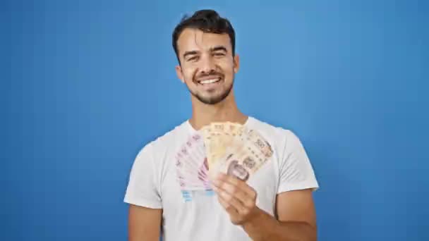 Młody Hiszpan Uśmiecha Się Pewnie Trzymając Meksykańskie Peso Odizolowanym Niebieskim — Wideo stockowe