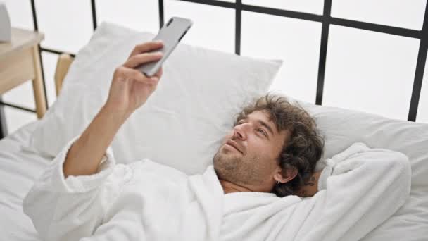 Bornoz Giyen Genç Spanyol Adam Yatak Odasında Gülümseyen Akıllı Telefon — Stok video