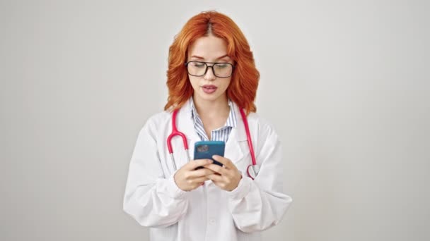 Młoda Ruda Kobieta Lekarz Uśmiecha Się Pomocą Smartfona Izolowanym Białym — Wideo stockowe