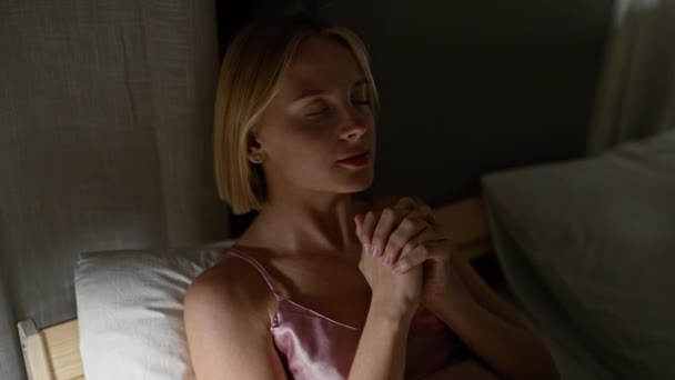ベッドに座って寝室で祈っている若い金髪の女性 — ストック動画