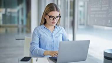 Genç sarışın iş kadını. Laptop kullanıyor. Ofiste çalışırken gözlük takıyor.