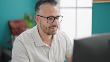 Gri saçlı iş adamı ofiste kutlama için bilgisayar kullanıyor.