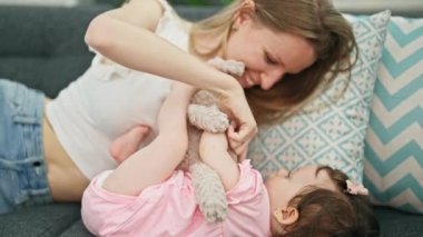 Anne ve kız kanepede uzanıp evde oyuncak ayıyla oynuyorlar.