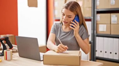 Genç sarışın kadın ecommerce iş işçisi. Ofiste paket üzerinde akıllı telefon yazısıyla konuşuyor.