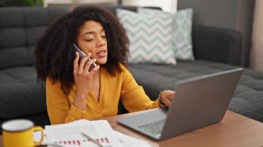 Akıllı telefondan konuşan Afrikalı Amerikalı kadın evde çalışırken notlar alıyor.