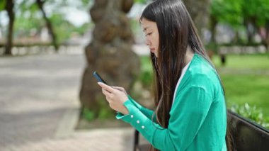 Parkta akıllı telefon kullanan genç Çinli bir kadın.