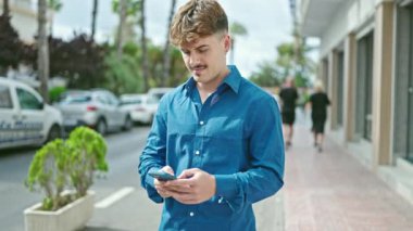 Young hispanic man using smartphone with winner gesture at street