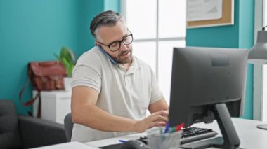 Gri saçlı iş adamı. Ofiste bilgisayarla konuşuyor.