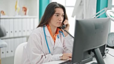 Genç, güzel İspanyol kadın doktor. Klinikte telefonla konuşan bilgisayar kullanıyor.