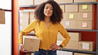 Afro-amerikan kadın ecommerce işçisi elinde bir paket ile ofise gülümsüyor.