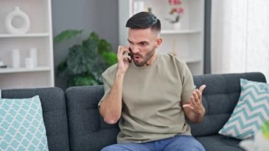 Genç İspanyol adam akıllı telefonda tartışıyor. Evdeki kanepede oturuyor.