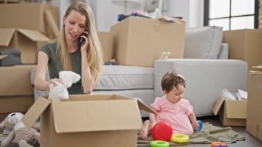 Anne ve kızı karton kutuda oyuncak paketliyor. Yeni evde akıllı telefondan konuşuyorlar.