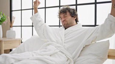 Genç İspanyol adam yatak odasında kollarını esneterek uyanıyor.