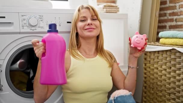 洗剤ボトルとブタバンを持っている洗濯室で服を洗う若い金髪女性 — ストック動画