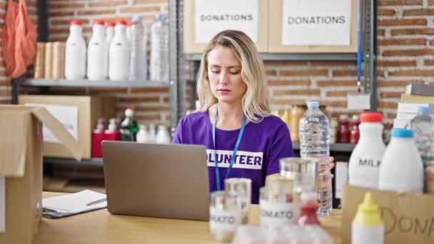 年轻的金发女性志愿者在慈善中心用笔记本电脑检查食物 — 图库视频影像