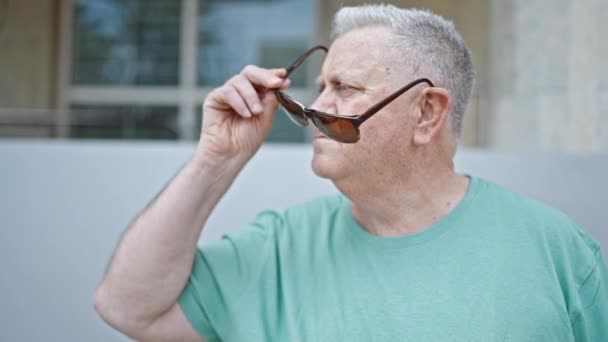 中年人灰白头发的男人带着自信的笑容在街上拿出太阳镜 — 图库视频影像
