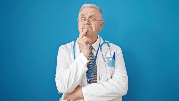 中年白髪の男医師立っています疑い表現思考上の隔離された青の背景 — ストック動画