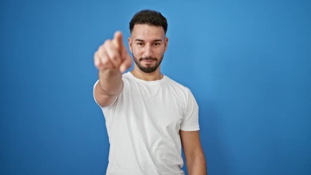 年轻的阿拉伯男子带着自信的微笑 用手指指向孤立的蓝色背景上的摄像机 — 图库视频影像