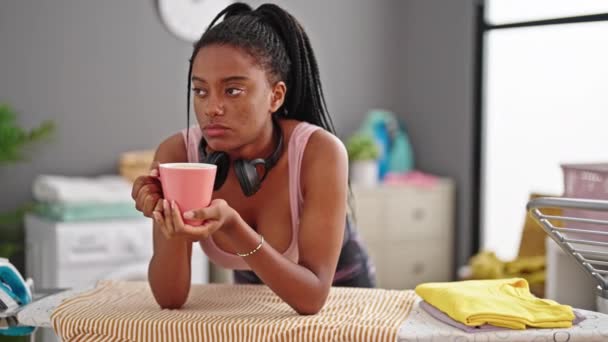 Mujer Afroamericana Bebiendo Café Apoyada Tabla Planchar Cansada Lavandería — Vídeo de stock
