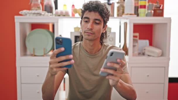 Jovem Hispânico Segurando Smartphones Sentados Mesa Sala Jantar — Vídeo de Stock