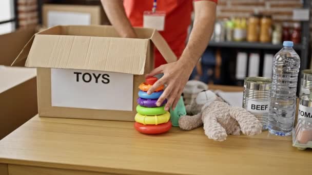 慈善センターで寄付パッケージにおもちゃを詰め若いヒスパニック系の男性ボランティア — ストック動画