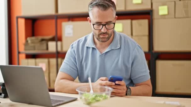 在办公室使用笔记本电脑和智能手机吃沙拉的白发男士电子商务业务 — 图库视频影像