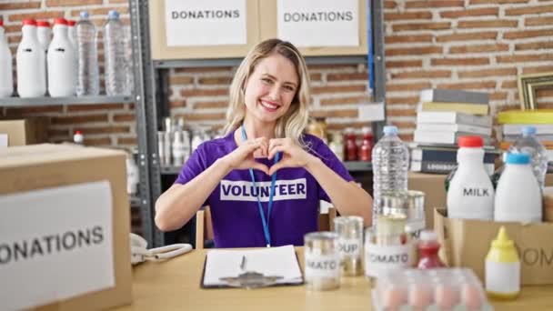 Jovem Loira Voluntária Sentada Mesa Fazendo Gesto Coração Centro Caridade — Vídeo de Stock