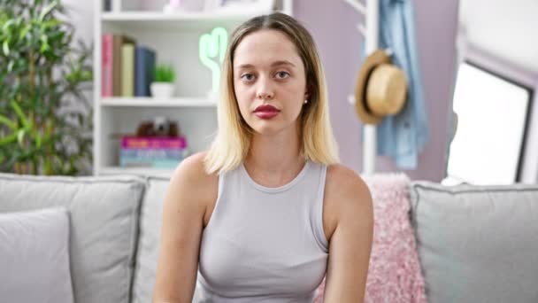 Mujer Rubia Joven Sentada Sofá Sorprendida Cubriendo Boca Con Las — Vídeo de stock