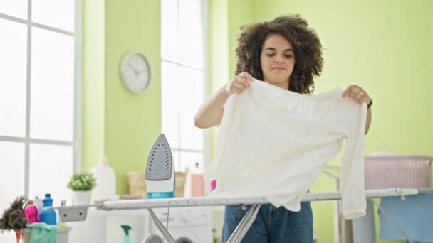 年轻美丽的惊慌失措的女人手挽着T恤在洗衣房微笑着熨烫衣服 — 图库视频影像