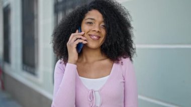 Afro-Amerikalı kadın gülümsüyor. Akıllı telefondan konuşuyor.