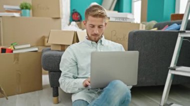 Genç beyaz adam dizüstü bilgisayar kullanıyor. Yeni evinde yerde oturuyor.