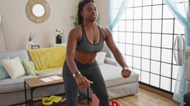Spor kıyafeti giyen Afrikalı Amerikalı kadın evde bacak egzersizi yapıyor.