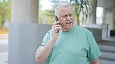 Middle age grey-haired man talking on smartphone with serious expression at street