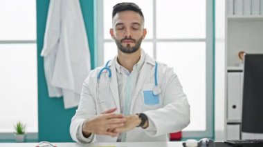 Masada oturan genç İspanyol doktor ciddi bir ifadeyle kliniği işaret ediyor.